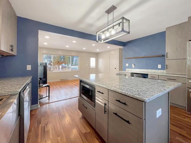 kitchen with light stone countertops, a center island, hanging light fixtures, appliances with stainless steel finishes, and hardwood / wood-style flooring