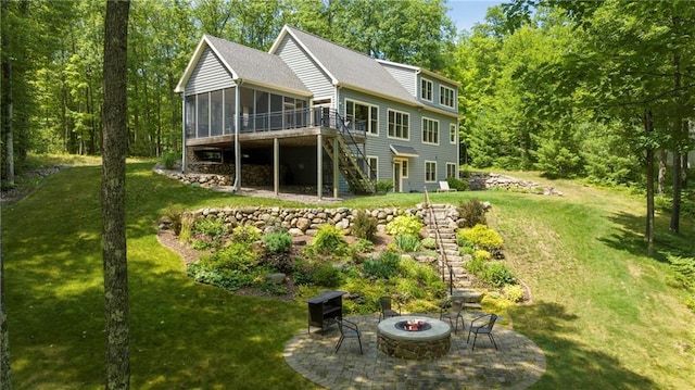 rear view of house with a lawn, a sunroom, a fire pit, a wooden deck, and a patio