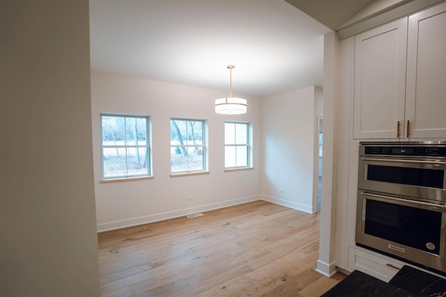 kitchen with double oven, hanging light fixtures, white cabinets, and light hardwood / wood-style floors