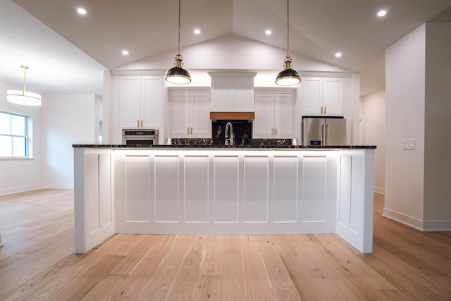 kitchen featuring white cabinets, stainless steel appliances, hanging light fixtures, and an island with sink