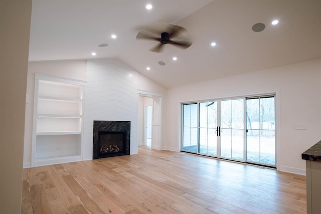 unfurnished living room with built in shelves, ceiling fan, a high end fireplace, lofted ceiling, and light wood-type flooring