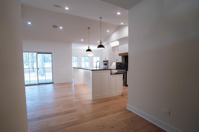 kitchen with white cabinets, vaulted ceiling, hanging light fixtures, and an island with sink