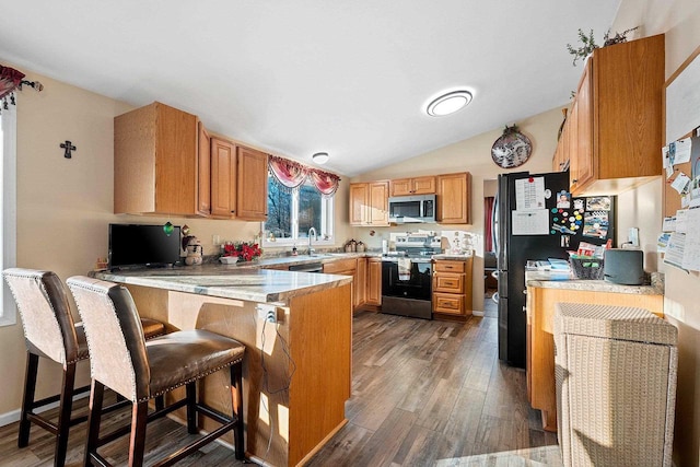 kitchen with sink, dark hardwood / wood-style floors, appliances with stainless steel finishes, kitchen peninsula, and a breakfast bar area