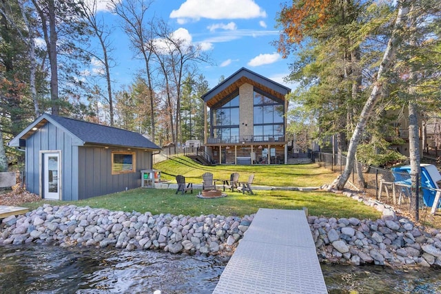 rear view of property with a water view, an outdoor structure, and an outdoor fire pit