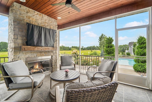 sunroom / solarium featuring an outdoor stone fireplace, ceiling fan, and wooden ceiling