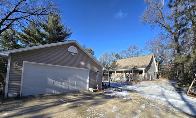 snow covered property with a garage, covered porch, and an outdoor structure