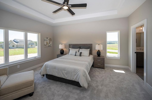 carpeted bedroom with ceiling fan, a raised ceiling, and ensuite bath