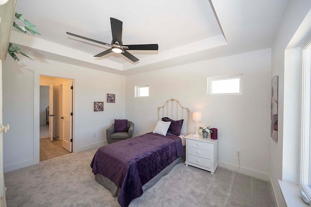 carpeted bedroom with a raised ceiling, multiple windows, and ceiling fan