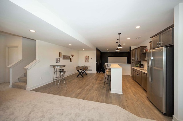 kitchen with stainless steel refrigerator with ice dispenser, a breakfast bar, dark brown cabinets, pendant lighting, and a kitchen island