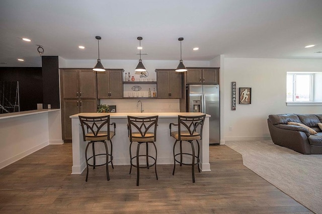 kitchen featuring a breakfast bar area, stainless steel fridge with ice dispenser, an island with sink, and pendant lighting