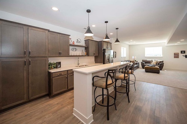 kitchen with sink, hanging light fixtures, stainless steel fridge with ice dispenser, a breakfast bar, and a kitchen island