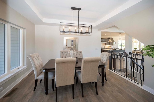 dining space featuring a raised ceiling, sink, dark hardwood / wood-style floors, and a notable chandelier