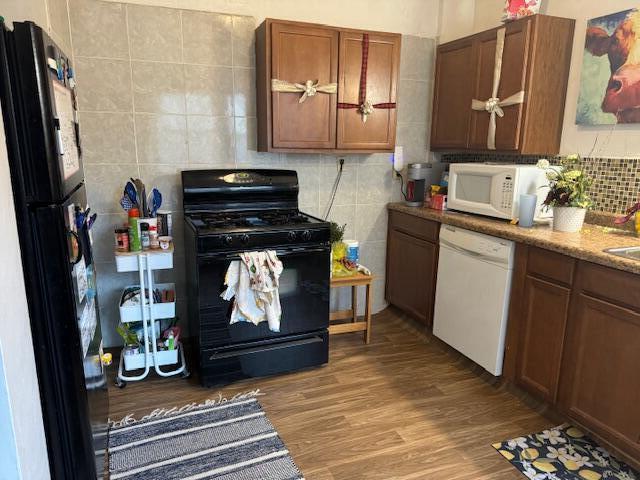 kitchen with hardwood / wood-style flooring, light stone counters, and black appliances