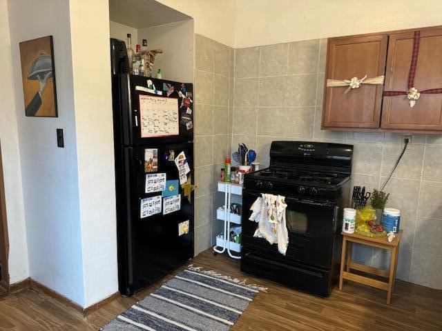 kitchen with tile walls, dark wood-type flooring, and black appliances