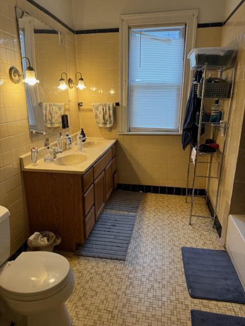 bathroom featuring a bathing tub, tile patterned flooring, toilet, vanity, and tile walls