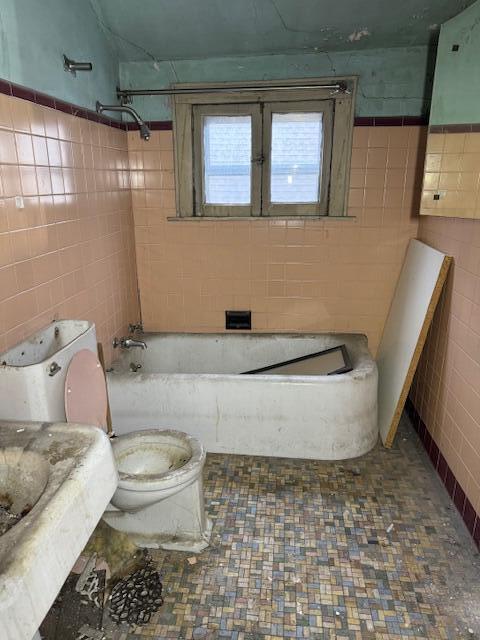 bathroom with washtub / shower combination, toilet, and tile walls