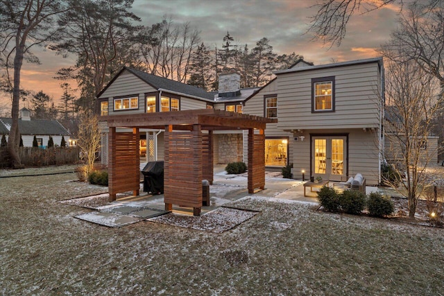 back house at dusk featuring a yard and a patio