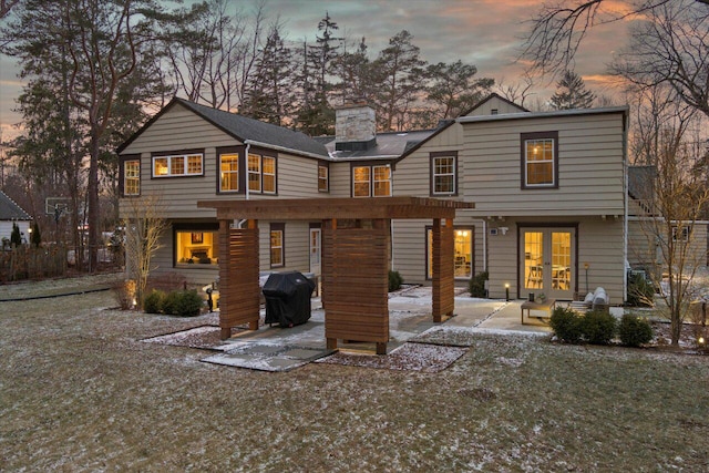 back house at dusk featuring a lawn, a patio, and french doors