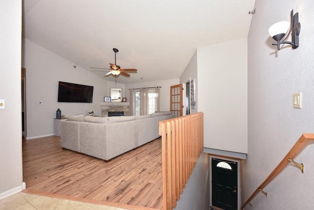 living room featuring ceiling fan, a stone fireplace, light wood-type flooring, and vaulted ceiling