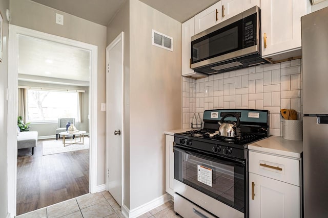 kitchen with white cabinets, light tile patterned floors, appliances with stainless steel finishes, and tasteful backsplash