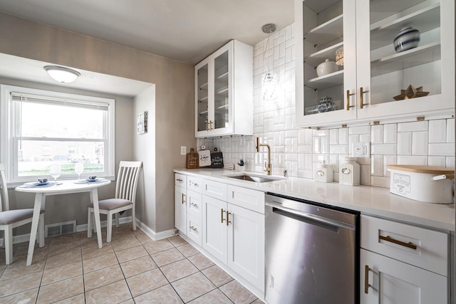 kitchen with tasteful backsplash, stainless steel dishwasher, sink, light tile patterned floors, and white cabinets