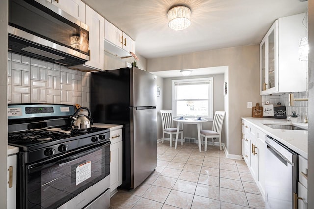 kitchen with white cabinets, appliances with stainless steel finishes, backsplash, and light tile patterned floors