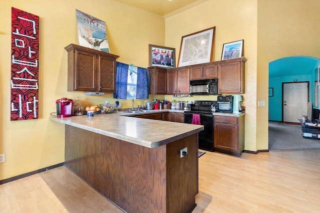 kitchen with sink, light hardwood / wood-style flooring, kitchen peninsula, a towering ceiling, and black appliances