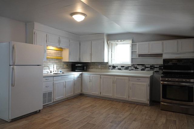 kitchen with gas range, sink, white fridge, lofted ceiling, and white cabinets