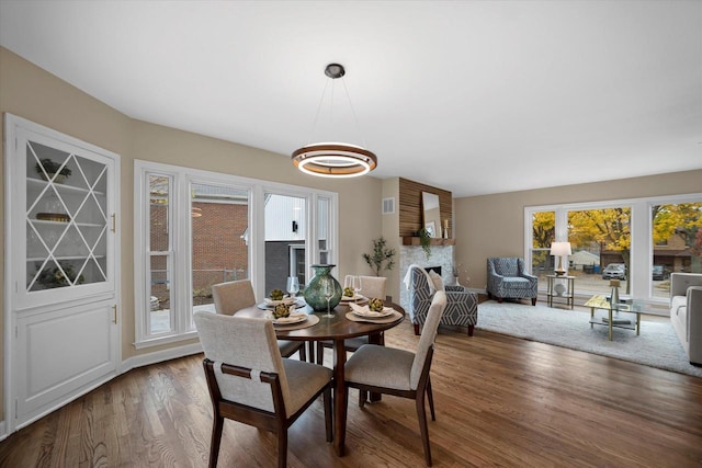 dining space with a wealth of natural light, a large fireplace, and dark hardwood / wood-style floors