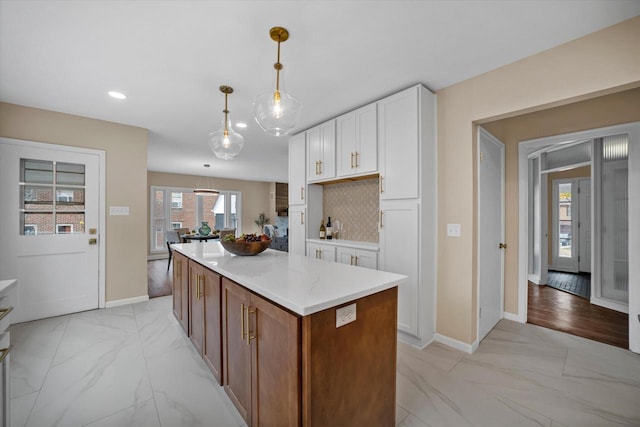 kitchen featuring a center island, decorative backsplash, decorative light fixtures, light stone counters, and white cabinetry