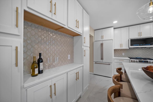 kitchen featuring white cabinetry, tasteful backsplash, light stone counters, decorative light fixtures, and white appliances