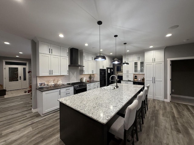 kitchen with white cabinets, stainless steel stove, a spacious island, and wall chimney range hood