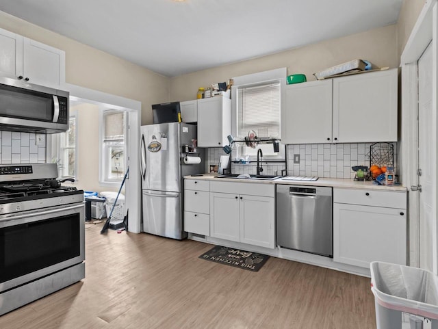 kitchen with sink, decorative backsplash, light wood-type flooring, white cabinetry, and stainless steel appliances