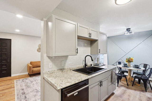 kitchen with light stone counters, light hardwood / wood-style floors, stainless steel dishwasher, and sink