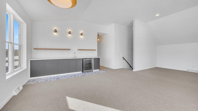 unfurnished living room with light colored carpet, wine cooler, and lofted ceiling