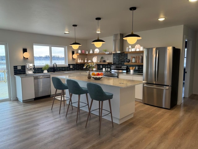 kitchen featuring backsplash, stainless steel appliances, wall chimney range hood, light hardwood / wood-style floors, and white cabinetry