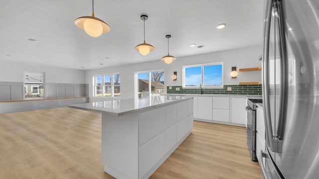 kitchen with decorative backsplash, stainless steel appliances, decorative light fixtures, light hardwood / wood-style flooring, and white cabinets