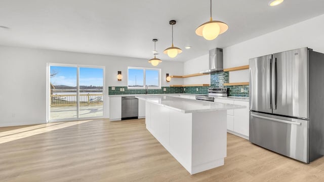 kitchen featuring pendant lighting, white cabinets, wall chimney exhaust hood, appliances with stainless steel finishes, and a kitchen island