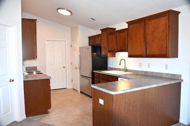 kitchen with kitchen peninsula, stainless steel fridge, vaulted ceiling, sink, and range