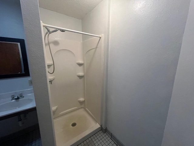 bathroom featuring tile patterned flooring, a textured ceiling, walk in shower, and sink