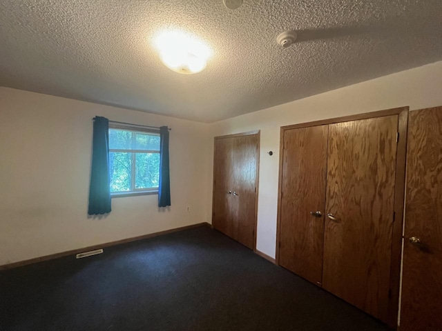 unfurnished bedroom with multiple closets, a textured ceiling, and dark colored carpet