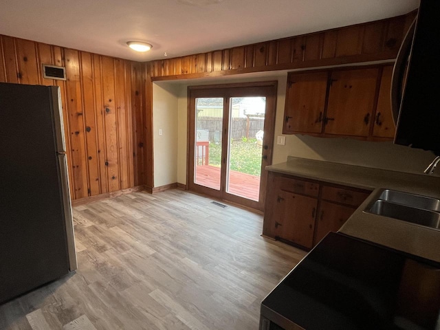 kitchen with wood walls, stainless steel fridge, sink, and light wood-type flooring