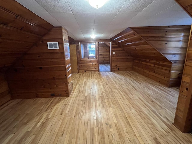 bonus room with vaulted ceiling, light wood-type flooring, and wood walls