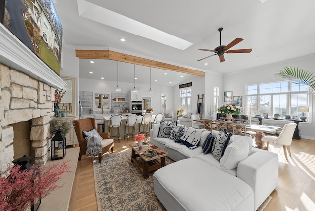 living room with light wood-type flooring, a skylight, ceiling fan, crown molding, and a fireplace