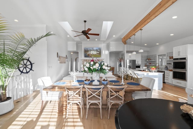 dining area with light hardwood / wood-style floors, lofted ceiling with skylight, ceiling fan, and sink