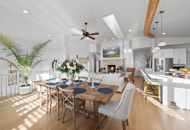 dining room with vaulted ceiling with skylight, ceiling fan, a fireplace, and light wood-type flooring