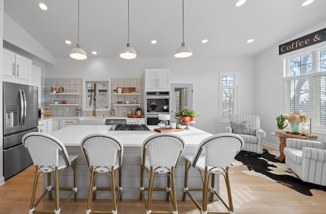 kitchen featuring backsplash, white cabinets, light wood-type flooring, appliances with stainless steel finishes, and decorative light fixtures