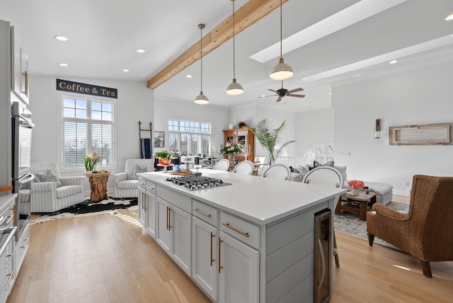 kitchen with hanging light fixtures, a kitchen breakfast bar, light hardwood / wood-style flooring, beamed ceiling, and stainless steel gas stovetop