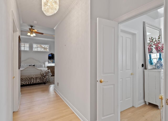 hallway with crown molding, light hardwood / wood-style flooring, a healthy amount of sunlight, and an inviting chandelier