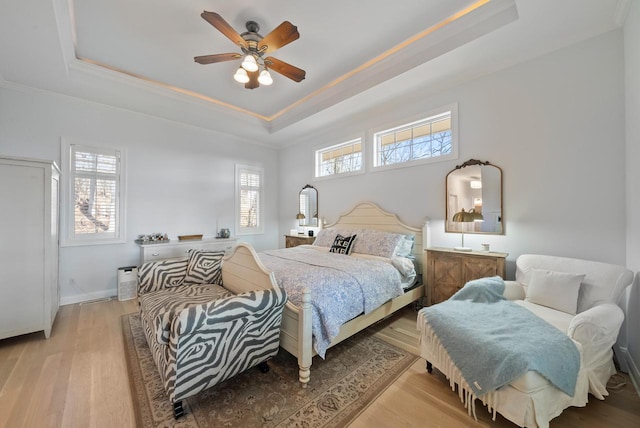 bedroom with a tray ceiling, multiple windows, ceiling fan, and light wood-type flooring